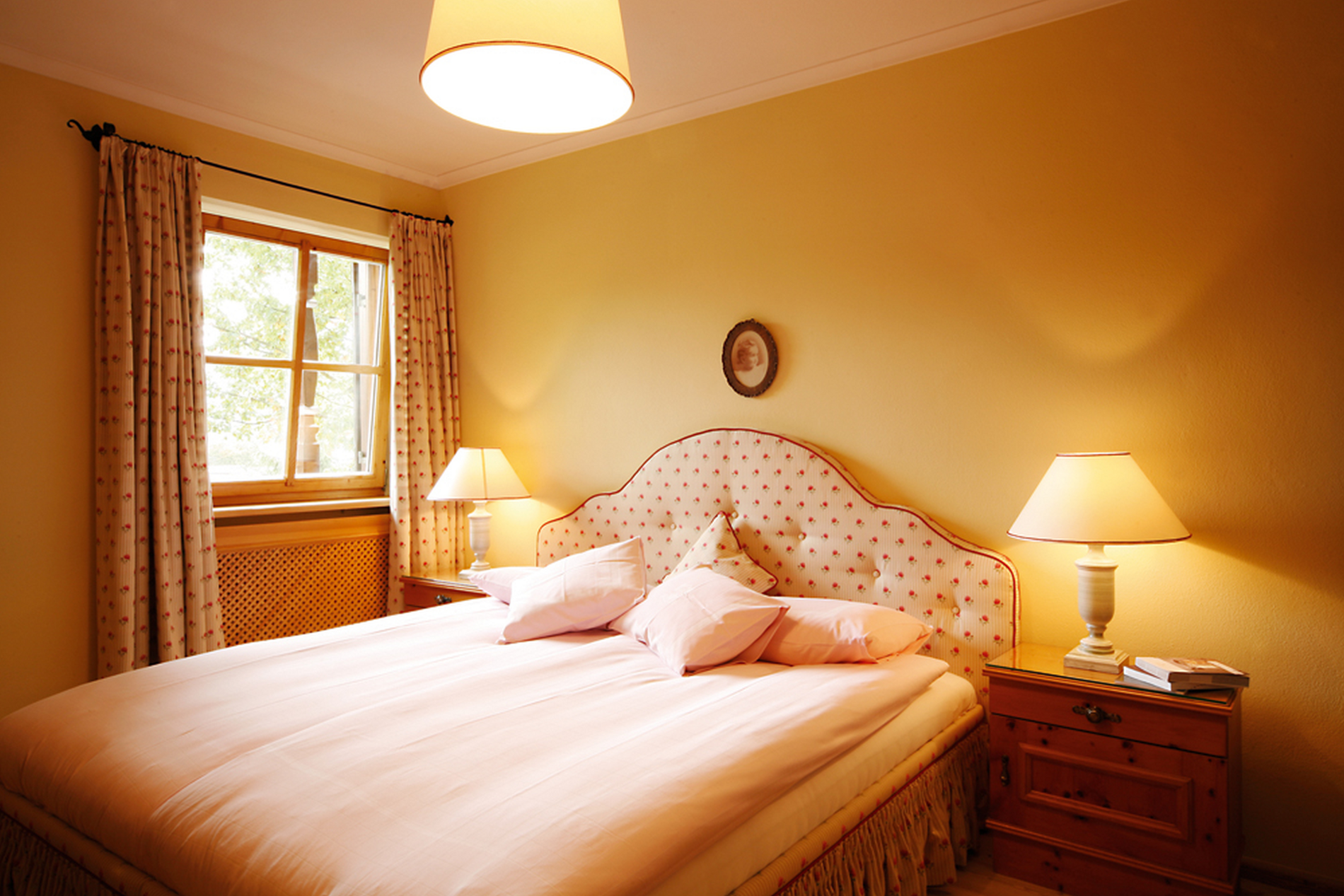 Gemütliches Schlafzimmer mit einem Doppelbett, Nachttischen, zwei Lampen und einem Fenster mit Vorhängen.