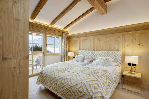Cozy wooden bedroom with large bed, patterned bed linen, soft lighting and mountain views through the windows.