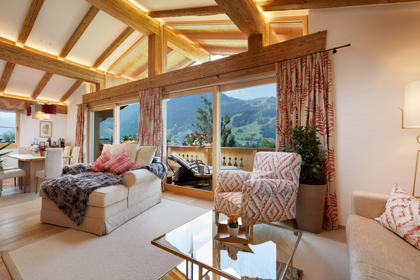 Cozy living room with large windows, mountain views, wooden beams and comfortable, stylish furniture.