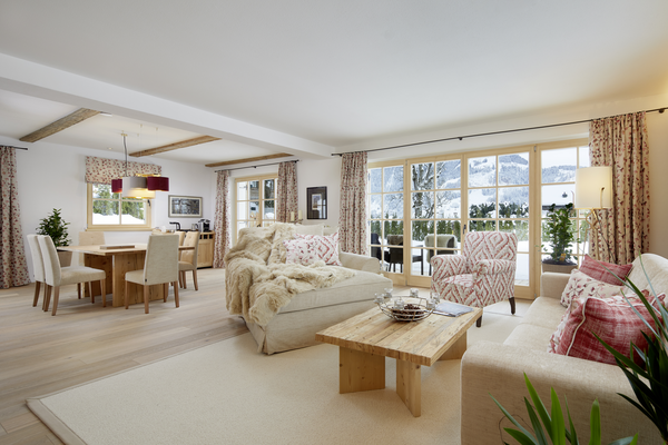 Bright, cozy living and dining area with large windows, wooden furniture and mountain views in the background.