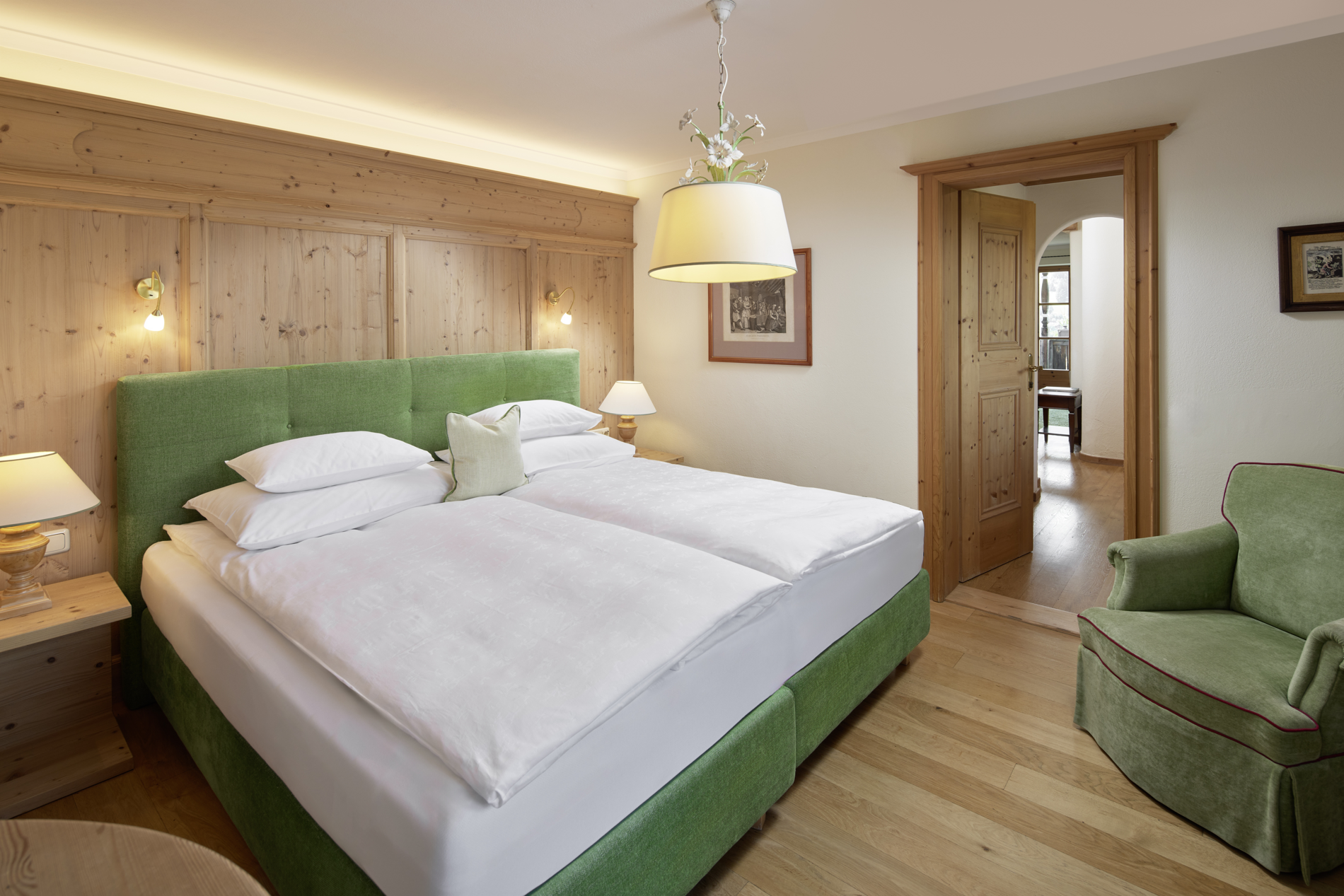 Ein gemütliches Hotelzimmer mit einem grünen Bett, hölzernen Akzenten und einem Sessel, beleuchtet von warmem, weichem Licht.