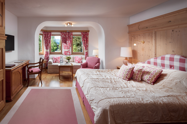 Comfortable hotel room with large bed, pink accents, sitting area, desk and view of the greenery from the window.